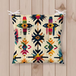 May include: Square cushion with a cream background and a colorful geometric pattern. The design features various shapes in shades of red, blue, yellow, and green. White ties are attached to the corners.