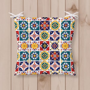 May include: Square seat cushion featuring a colourful, repeating tile pattern in red, yellow, blue, and teal. The cushion has white ties at each corner. The design is reminiscent of traditional tilework.