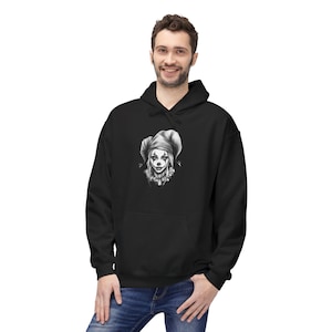 May include: Black hoodie featuring a detailed grayscale illustration of a jester's face on the front. The jester has a pointed hat and a sinister smile. The hoodie has a front pocket and a drawstring hood. The model is wearing blue jeans.