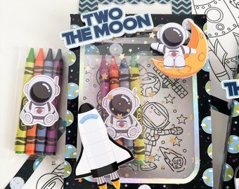 May include: A black and white coloring book set with an astronaut theme. The set includes a coloring book, crayons, and stickers. The coloring book features an astronaut on the moon, a rocket ship, and planets. The stickers feature an astronaut, a rocket ship, and a moon.