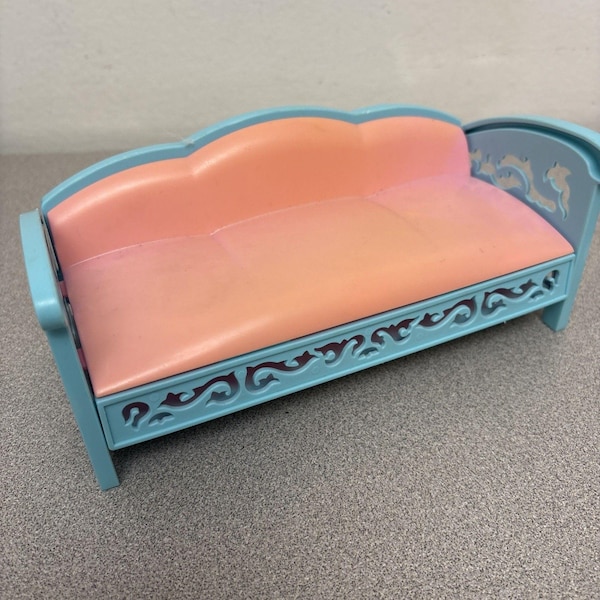 May include: A miniature dollhouse sofa featuring a smooth, peach-colored seat and backrest. The frame is light blue with an intricate, cut-out scrollwork pattern along the front base and the side armrest, providing a decorative, open-work design.