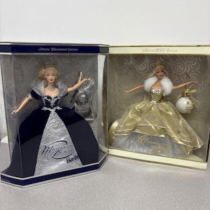 May include: Two Barbie dolls in display boxes. One doll wears a navy blue gown with silver accents, labeled "Millennium Princess Barbie." The other doll is in a gold gown, labeled "Special 2000 Edition." Both dolls have blonde hair and are in clear plastic cases.