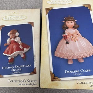Peut inclure: Deux boîtes d'ornements Hallmark Keepsake. L'une présente une poupée en tenue de patineuse rouge et blanche, intitulée "Holiday Snowflake Skater". L'autre montre une poupée en robe rose, intitulée "Dancing Clara".