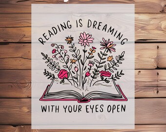 May include: A DTF transfer design featuring an open book with flowers and the text "Reading is dreaming with your eyes open." The design includes pink, yellow, and black elements. The words "Ready To Press" and "DTF Transfer" are also included.