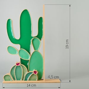 May include: A decorative cactus-shaped bookend. The bookend is green with a gold outline and measures 7.5 inches tall, 5.5 inches wide, and 1.8 inches deep. The cactus design features a variety of shapes and sizes, with small red accents.