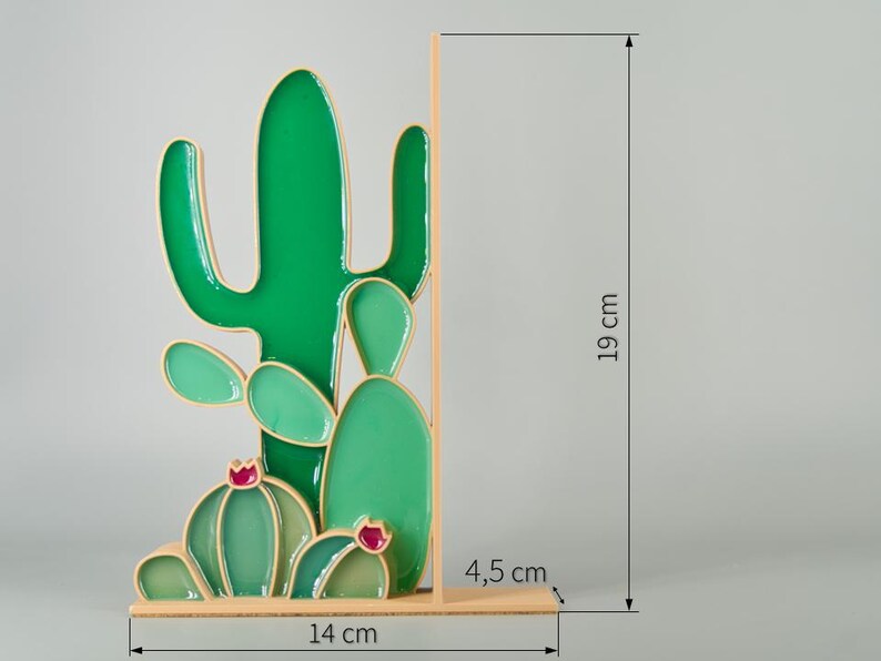 May include: A decorative cactus-shaped bookend. The bookend is green with a gold outline and measures 7.5 inches tall, 5.5 inches wide, and 1.8 inches deep. The cactus design features a variety of shapes and sizes, with small red accents.