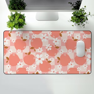 Puede incluir: Alfombrilla de ratón rectangular con un patrón de melocotones y flores sobre un fondo a cuadros rosa y blanco. El diseño presenta melocotones estilizados y flores blancas. Un ratón de ordenador blanco está en el lado derecho.