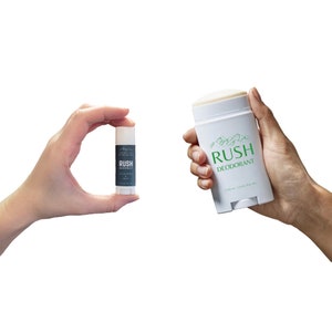 May include: Two hands holding two different sizes of white deodorant sticks. The larger stick has a green mountain design and the text "RUSH DEODORANT". The smaller stick has a black label with the text "RUSH EUCALYPTUS &  MINT".
