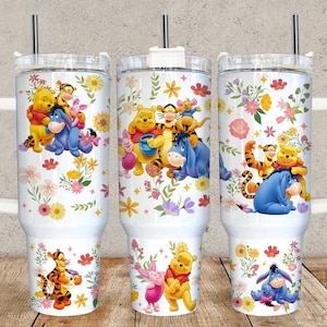 Puede incluir: Tres vasos térmicos blancos con asas, cada uno con un diseño colorido de Winnie the Pooh y sus amigos. El diseño incluye a Pooh, Piglet, Tigger, Eeyore y flores. Cada vaso tiene una pajita plateada.
