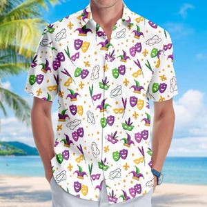 Könnte beinhalten: Weißes kurzärmeliges Hemd mit einem sich wiederholenden Muster aus Mardi Gras-Masken, Narrenhüten, Fleur-de-Lis und Perlenketten in Lila, Grün und Gold. Das Hemd wird von einer Person am Strand getragen.