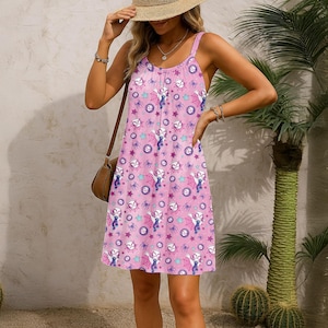 May include: A pink spaghetti strap dress featuring a repeating pattern of a cartoon character, spiderwebs, stars, and circles. The dress has a scoop neckline and a knee-length hemline. The dress is made of a lightweight fabric.