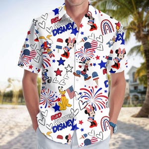 Może przedstawiać: Biała koszula zapinana na guziki z patriotycznym motywem Disneya. Koszula przedstawia Myszki Miki i Minnie, Pluto, fajerwerki, gwiazdy i rożki lodów w kolorach czerwonym, białym i niebieskim. Widoczny jest również napis "Red White & Disney".