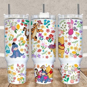 Puede incluir: Tres vasos aislados blancos con asas, con estampados florales y personajes de dibujos animados. Los personajes incluyen Winnie the Pooh, Tigger, Piglet y Eeyore. Cada vaso tiene una tapa transparente y una pajita de acero inoxidable.