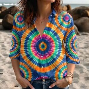 May include: A long-sleeved button-down shirt with a vibrant tie-dye pattern. The shirt features concentric circles in shades of blue, orange, green, and pink. The shirt is unbuttoned at the top, revealing a glimpse of a necklace.