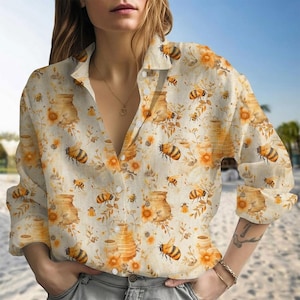 May include: A button-down shirt with a bee and honeycomb pattern. The long-sleeved shirt features a cream background with orange and yellow bees, honeycombs, and floral accents. The shirt has a classic collar and button closure.