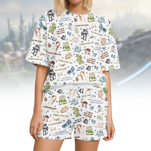 May include: White pajama set featuring a repeating pattern of Star Wars characters and quotes. The set includes a short-sleeved top and matching shorts with a drawstring waist. The design incorporates various characters and phrases from the Star Wars franchise.