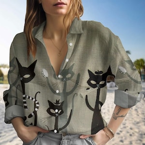 以下が含まれることがあります： 緑色のボタンダウンシャツ。スタイリッシュな黒猫の繰り返し模様が特徴です。猫は様々なポーズで描かれており、アクセサリーを身につけているものもあります。長袖のシャツには襟とボタンが付いています。