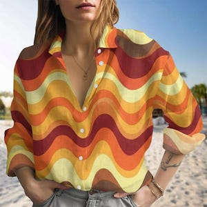 Puede incluir: Camisa abotonada de manga larga con un estampado retro de ondas en tonos naranja, amarillo y marrón. La camisa tiene cuello y botones blancos. La tela parece ligera.
