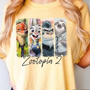 Puede incluir: Camiseta amarilla clara con un estampado colorido de personajes de Zootopia, incluyendo un zorro, un conejo, un gorila y un perezoso. El texto "Zootopia 2" est&aacute; escrito debajo de los personajes. La palabra "BUTTER" est&aacute; impresa en la esquina inferior derecha.