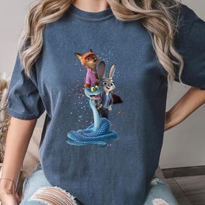 May include: Denim blue t-shirt with a colourful graphic of a fox, a rabbit, and a snake. The fox wears a pink shirt, and the rabbit wears a blue suit. The snake is blue. The word "DENIM" is printed on the bottom right.