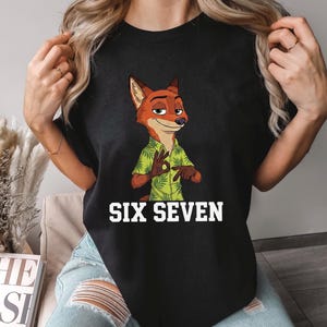 Puede incluir: Camiseta negra con un personaje de zorro de dibujos animados que lleva una camisa hawaiana verde. El texto "SIX SEVEN" est&aacute; impreso en blanco debajo de la imagen. La palabra "BLACK" est&aacute; impresa en blanco en la parte inferior derecha.