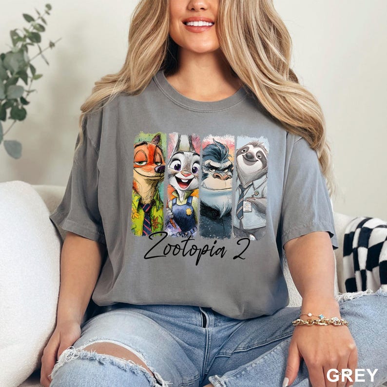Puede incluir: Camiseta gris con personajes de Zootopia 2. El dise&ntilde;o incluye a Nick Wilde, Judy Hopps, el Jefe Bogo y Flash, con el texto "Zootopia 2" debajo. La camiseta es de color gris liso.