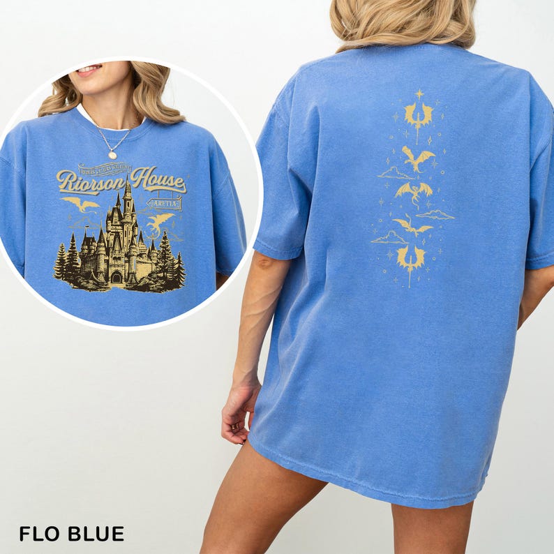 May include: Flo blue t-shirt with a gold graphic on the front featuring a castle and the text "Riorrson House". The back of the shirt has a gold dragon design. The shirt is a comfortable, oversized fit.