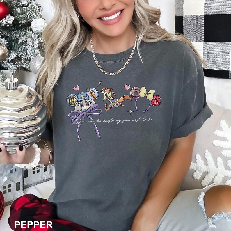 Puede incluir: Camiseta gris oscuro con un gr&aacute;fico colorido de personajes de dibujos animados y diademas. El texto "You can be anything you wish to be" est&aacute; impreso debajo. La camiseta tiene las mangas dobladas.