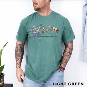 Puede incluir: Camiseta verde claro con un gr&aacute;fico de dibujos animados con personajes y accesorios. El gr&aacute;fico incluye un personaje con un lazo, una ardilla y una diadema en forma de rosquilla. Tambi&eacute;n se incluye el texto "You can be anything you wish to be".