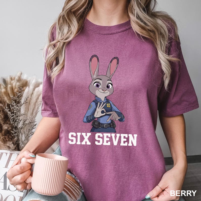 Puede incluir: Camiseta de color bayas con una imagen de dibujos animados de Judy Hopps de Zootopia, haciendo un gesto con la mano. El texto "SIX SEVEN" est&aacute; impreso en blanco debajo de la imagen. La camiseta es de estilo casual y c&oacute;modo.