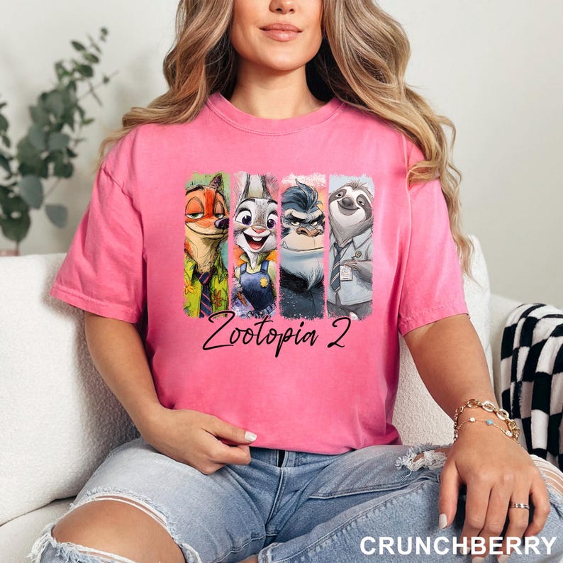 Puede incluir: Camiseta rosa con un dise&ntilde;o colorido de personajes de la pel&iacute;cula Zootopia. El dise&ntilde;o incluye a Nick Wilde, Judy Hopps, Jefe Bogo y Flash. El texto "Zootopia 2" est&aacute; escrito debajo de los personajes.