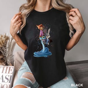 May include: Black t-shirt with a colourful graphic of Zootopia characters: Nick Wilde, Judy Hopps, and a blue snake. The word "BLACK" is printed at the bottom right of the shirt.
