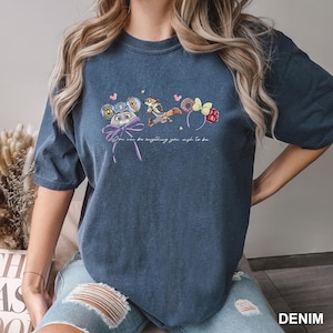 Puede incluir: Camiseta azul denim con un gr&aacute;fico caprichoso de diademas de personajes de dibujos animados y el texto "You can be anything you wish to be." El dise&ntilde;o incluye una diadema de orejas de rat&oacute;n, una ardilla y una diadema de frambuesa.