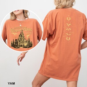 May include: Orange t-shirt with a graphic of a castle and the text "Rierson House" on the front. The back of the shirt features a vertical design with stylized dragons and clouds. The shirt is a comfortable, oversized fit.