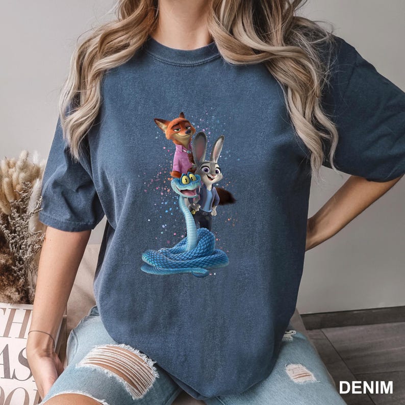 May include: Denim blue t-shirt with a colourful graphic of a fox, a rabbit, and a snake. The fox wears a pink shirt, and the rabbit wears a blue suit. The snake is blue. The word "DENIM" is printed on the bottom right.