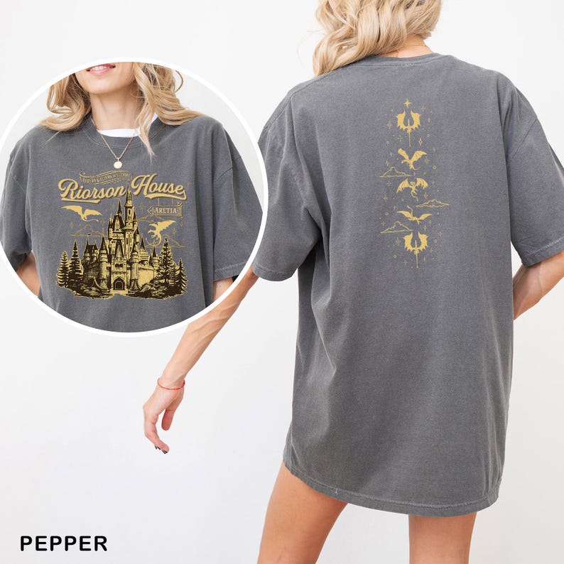 May include: Pepper-colored t-shirt with a graphic on the front featuring a castle, trees, and the text "Riorrson House". The back of the shirt has a gold dragon design. The shirt is a comfortable, oversized fit.