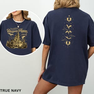 May include: True navy blue t-shirt with a gold graphic on the front featuring a castle and text that reads "Riorrson House". The back of the shirt has a gold dragon design. The shirt is a comfortable, casual style.