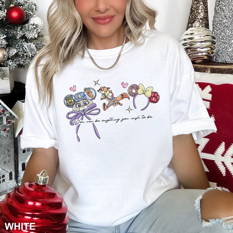 Puede incluir: Camiseta blanca con un gr&aacute;fico de dibujos animados de personajes y accesorios. El dise&ntilde;o incluye un rat&oacute;n con uniforme de polic&iacute;a, un zorro y diademas tem&aacute;ticas. Tambi&eacute;n se incluye el texto "You can be anything you wish to be".