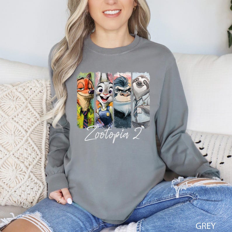 Puede incluir: Una camiseta gris de manga larga con un gr&aacute;fico colorido de personajes de la pel&iacute;cula "Zootopia 2". El gr&aacute;fico incluye a Nick Wilde, Judy Hopps, Duke Weaselton y Flash. El texto "Zootopia 2" est&aacute; escrito en blanco debajo.