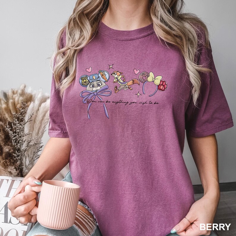 Puede incluir: Camiseta de color bayas con gr&aacute;ficos de personajes de dibujos animados y el texto "You can be anything you wish to be." El dise&ntilde;o incluye un lazo, corazones y estrellas. La camiseta es de material suave.