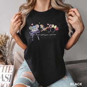 Puede incluir: Camiseta negra con un gr&aacute;fico colorido de orejas de personajes de dibujos animados y un lazo, con el texto "You can be anything you wish to be." El dise&ntilde;o incluye un rat&oacute;n, un zorro y elementos florales. La palabra "BLACK" est&aacute; impresa en la parte inferior.