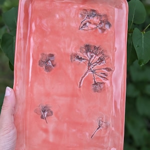 May include: A rectangular ceramic tray with a light pink glaze and pressed flower designs. The tray has a smooth, glossy finish.