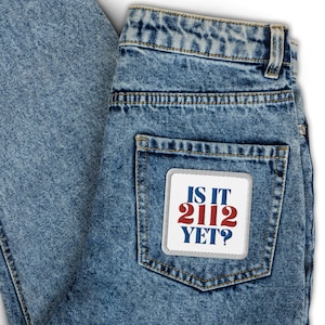 May include: A blue denim jean pocket with a white patch that says "IS IT 2112 YET?" in red, white, and blue lettering.