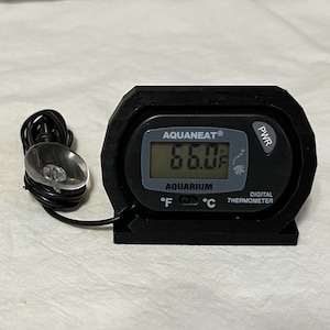 May include: Black digital aquarium thermometer with a suction cup and a probe. The display shows a temperature of 66.0 degrees Fahrenheit. The thermometer has a power button labeled "PWR" and a switch to toggle between Fahrenheit and Celsius.
