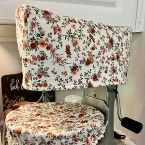 May include: A floral patterned cover set for a stand mixer. The set includes a top cover and a bowl cover, both featuring a white background with red, orange, and pink flowers and green leaves. The bowl cover has a lace trim.