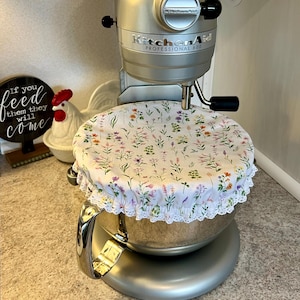 May include: A silver KitchenAid stand mixer with a white floral patterned bowl cover. The mixer has the words "KitchenAid Professional 600" printed on the side.