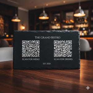 Peut inclure: Un panneau en ardoise noire pour un bistrot avec le texte "THE GRAND BISTRO" et deux codes QR. Le panneau indique "SCANNER POUR LE MENU" et "SCANNER POUR LES BOISSONS". Le panneau indique également "EST. 2023".