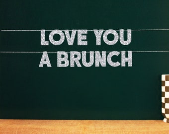 May include: A green chalkboard with the text "LOVE YOU A BRUNCH" written in silver glitter letters.