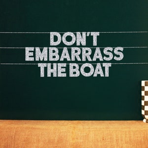 Op de afbeelding: Zilveren glitterletters die de zin "Don't Embarrass The Boat" spellen op een donkergroene schoolbordachtergrond.