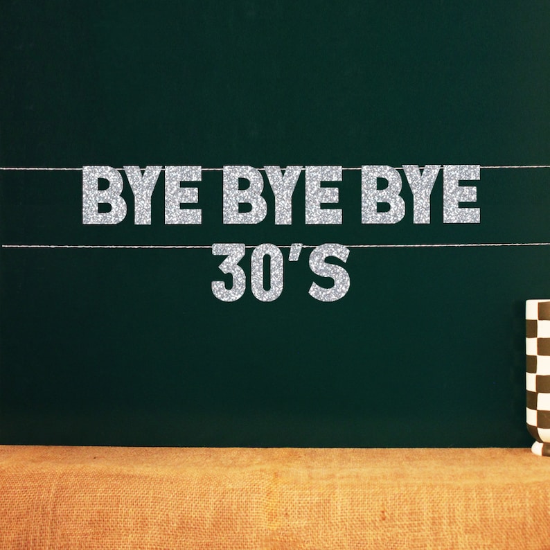 Puede incluir: Letras de purpurina plateada que deletrean "Bye Bye Bye 30's" sobre un fondo de pizarra verde oscuro.